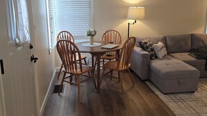 Un salon chaleureux avec un coin repas, un plancher en bois et un canapé gris.