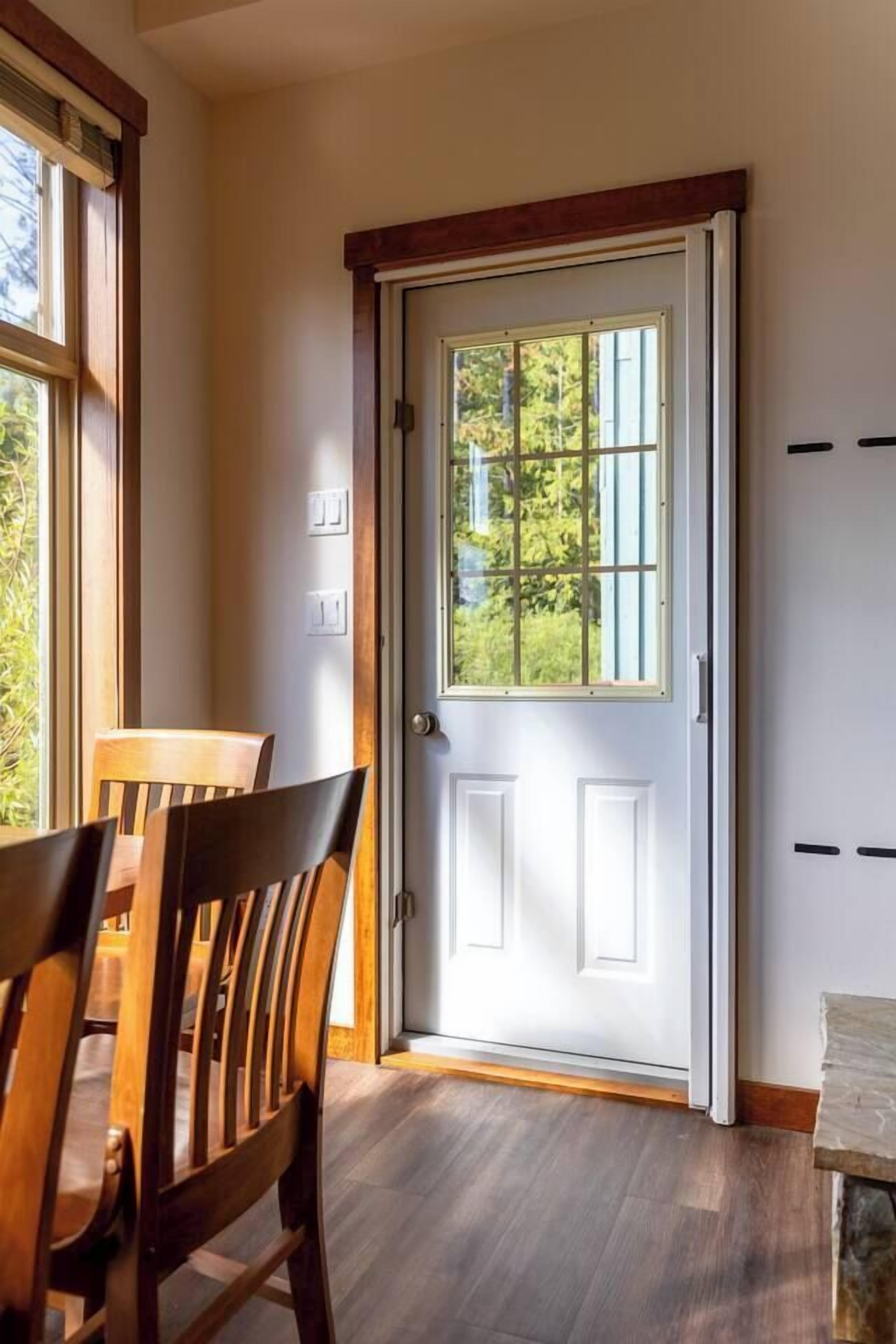 Une pièce comprenant une table et des chaises en bois, une porte blanche avec une fenêtre, et un élément décoratif en pierre sur le sol.