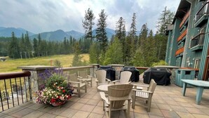 Eine Terrasse mit Gartenmöbeln, Blumen und Blick auf Berge und Bäume.