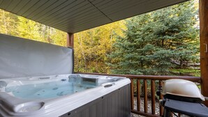 Un jacuzzi en una terraza de madera con vistas a un bosque.