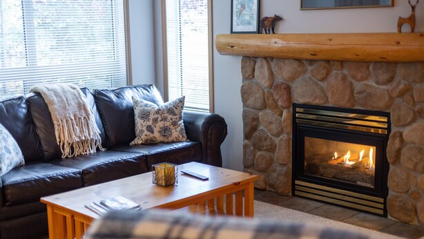 Una sala de estar acogedora con chimenea de piedra, un sofá de cuero con cojines y una mesa de centro de madera.