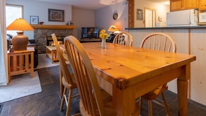 Una mesa de comedor de madera con sillas, una chimenea de piedra, un televisor y armarios de madera en una zona de estar acogedora.