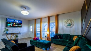 Ein Wohnzimmer mit Flachbildfernseher, grünen Sofas, einem Couchtisch und einem dekorativen Spiegel.