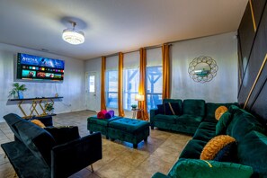 A living room with a flat-screen TV, green sofas, a coffee table, and a decorative mirror.