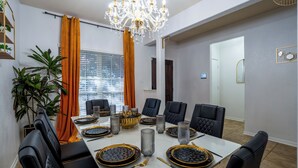 Ein Esszimmer mit weißem Tisch, schwarzen Stühlen, einer Chandelier und einer Pflanze.