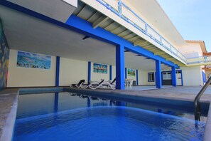 Une piscine dotée de chaises longues et d’un espace abrité où sont exposées des œuvres d’art.