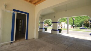 A covered outdoor area with a concrete floor, blue and white pillars, and a view of a street with cars and greenery. - Hotel Xestalito (Santa María Huatulco)