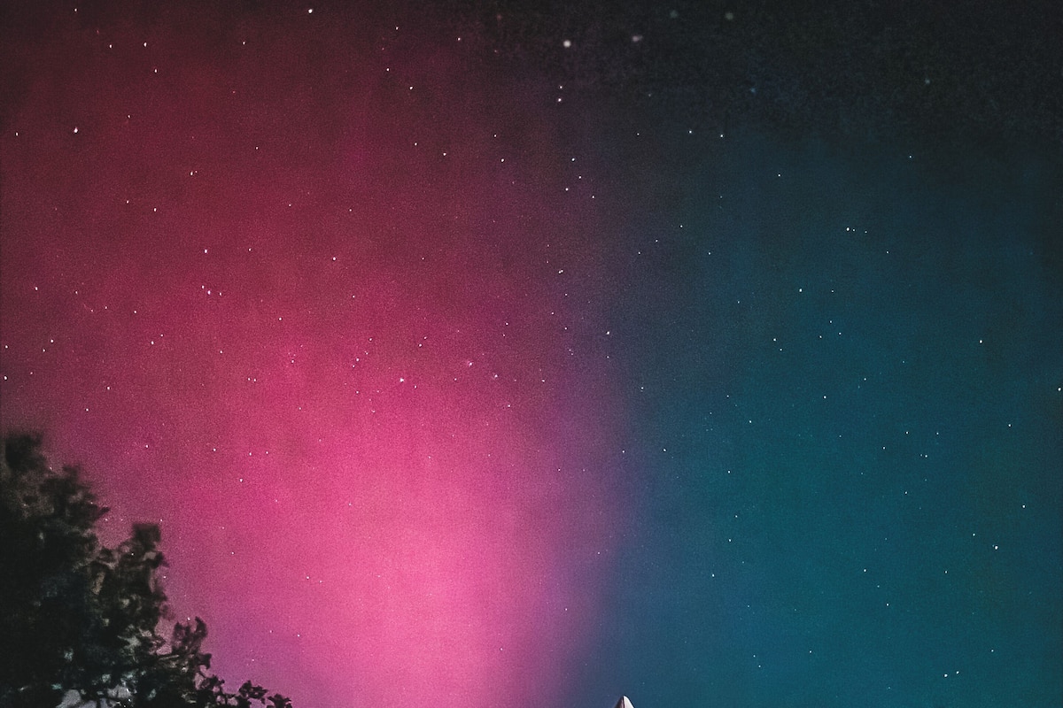A tent with a peaked roof, set against a night sky with visible stars and a vibrant aurora display.