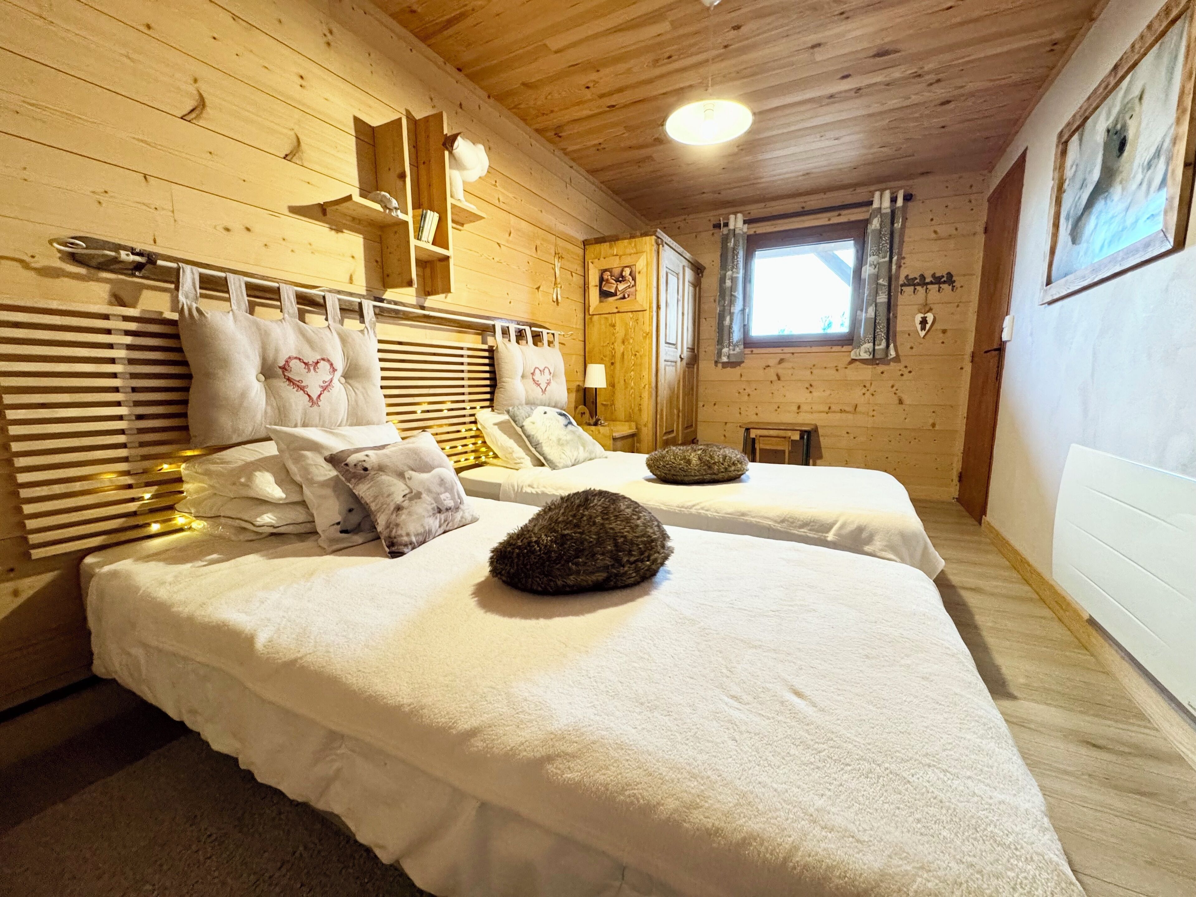 Une pièce chaleureuse avec deux lits, des murs en bois, une fenêtre avec des rideaux et un plafond en bois.
