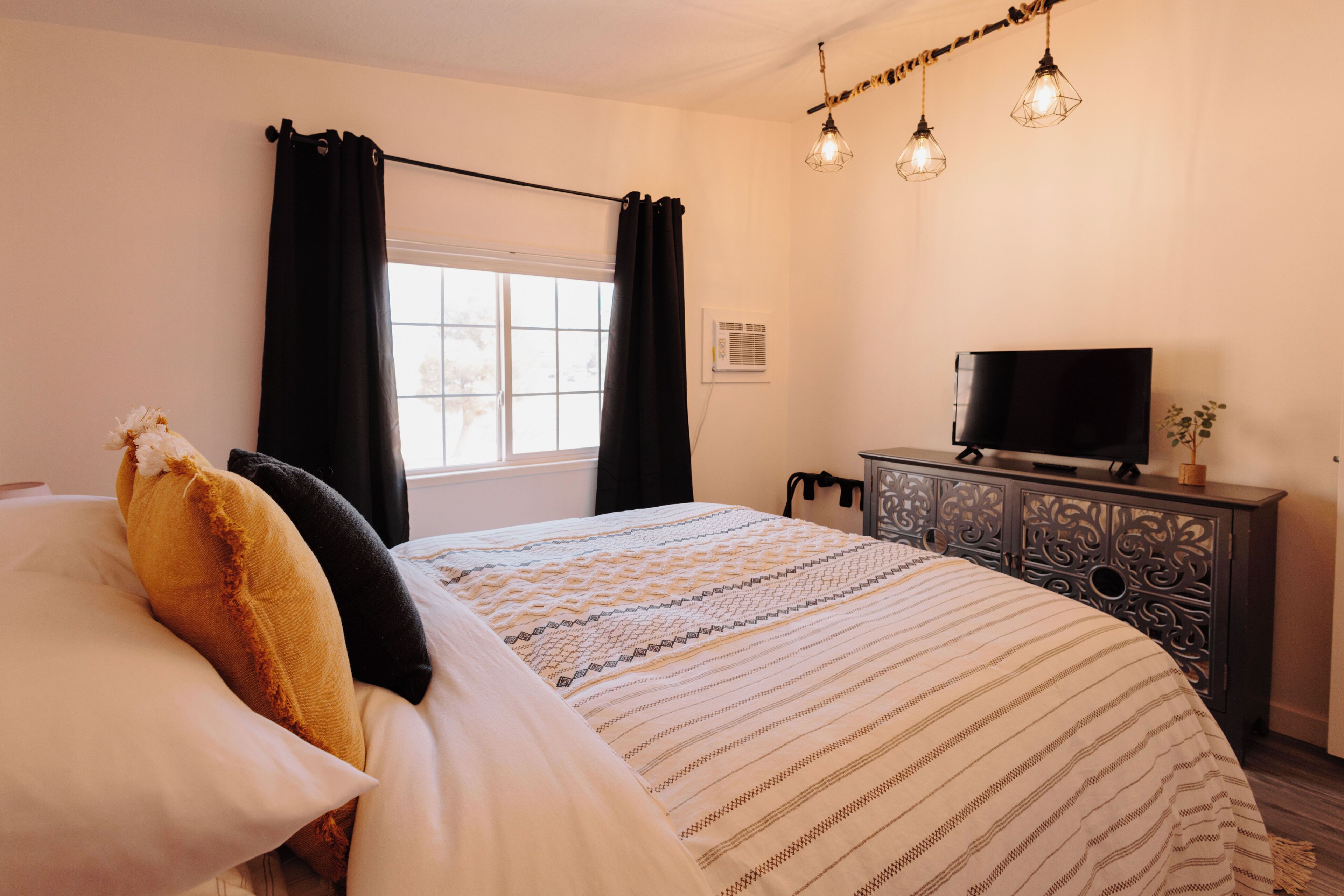 Ein Schlafzimmer mit einem Bett, schwarzen Vorhängen, einem Fernseher auf einem Schrank und einem Fenster.