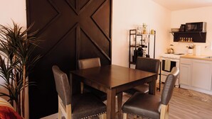 Ein Essbereich mit einem dunklen Holztisch und Stühlen, einem Deckenventilator und einer Küche im Hintergrund.