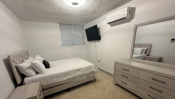 Quarto com cama, penteadeira, televisão e aparelho de ar condicionado.