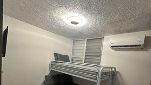 Quarto com beliche, lâmpada no teto, ar condicionado e uma porta.