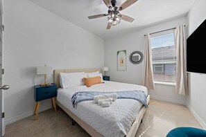 Un dormitorio con cama, mesitas de noche, ventilador de techo, ventana con persianas y espejo instalado en la pared.
