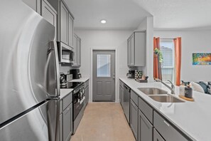 A modern kitchen with stainless steel appliances, a double sink, and a view to the living area. - Ideal for long-term stays-available for 14 days and Beyond. (Temple)