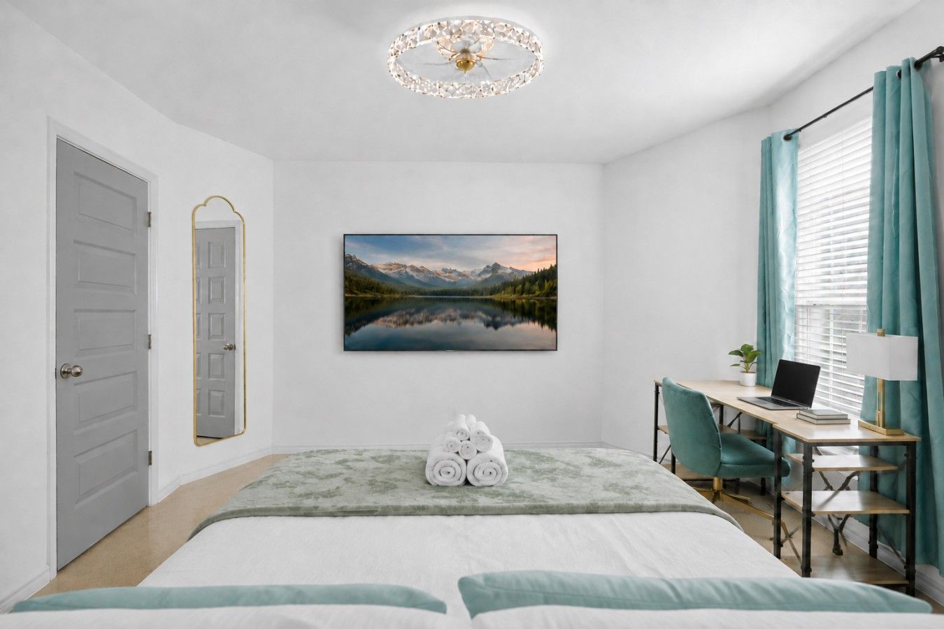 Une chambre à coucher avec un lit, un bureau avec un ordinateur portable, une chaise, un tableau représentant un paysage de montagne et une porte.