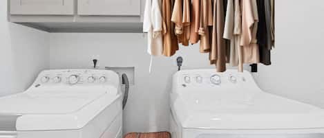 A laundry room with two washing machines, a drying rack with clothes, and a wooden laundry basket.