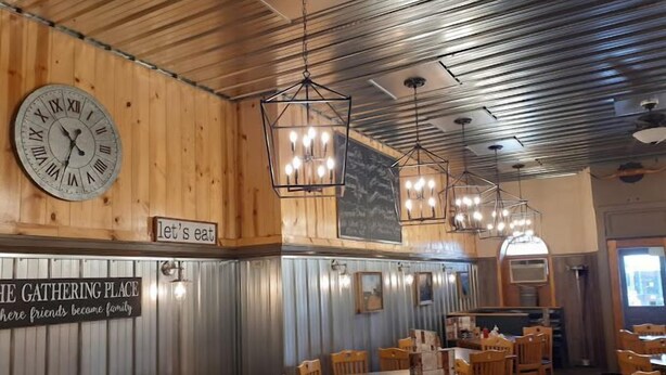Interior de restaurante con paredes de madera, un reloj grande, lámparas colgantes y mesas con sillas dispuestas para comer.
