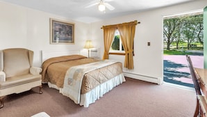 Un dormitorio con cama, una silla, ventilador de techo, ventana con cortinas y vistas al exterior.