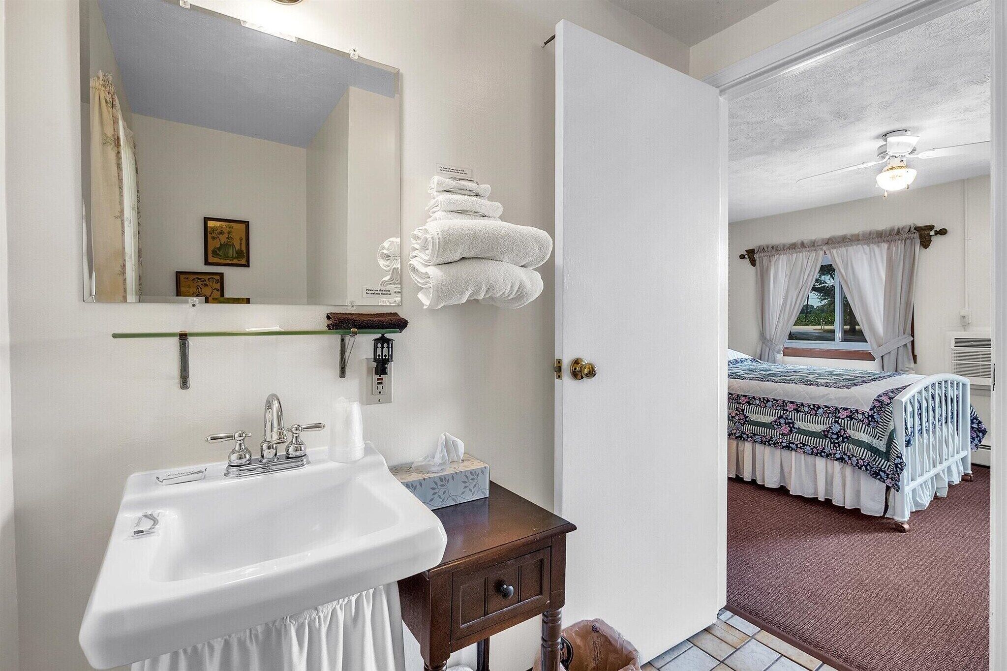 A bathroom with a sink, mirror, and towels stacked on a shelf.
