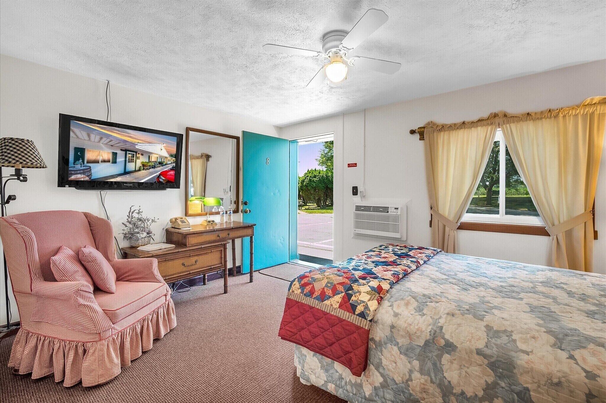 A bedroom with a bed, a chair, a desk, a television, and a window with curtains.