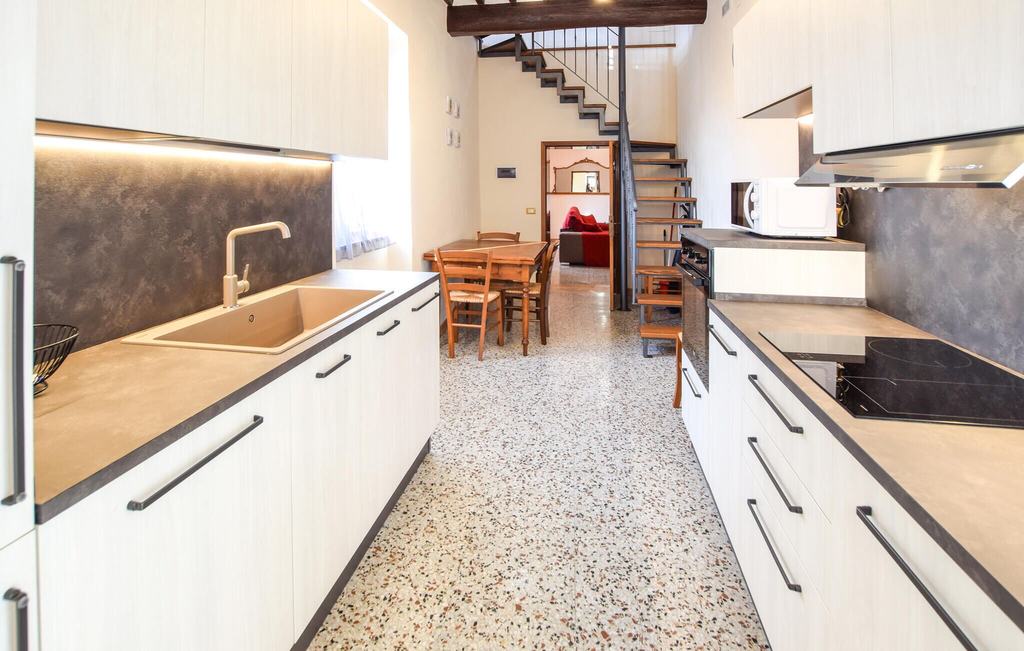 A modern kitchen with a central island, wooden cabinets, and a staircase leading to an upper level.