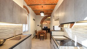 A narrow kitchen with a central island, a dining area with chairs, and a TV in the background.