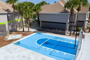 Un terrain de basket avec une surface bleue, entouré d’arbres et d’immeubles.