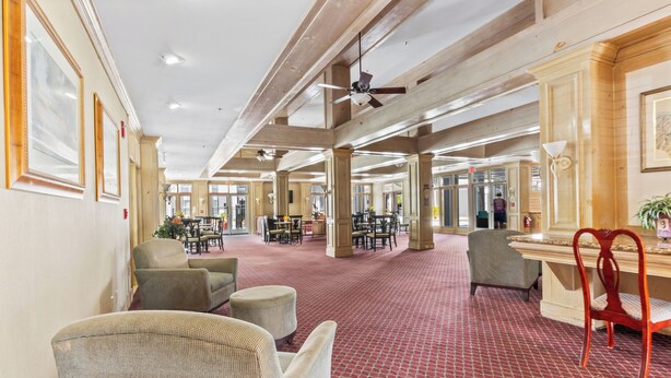 Un hall d’entrée spacieux avec de hauts plafonds, une moquette rouge à motifs et plusieurs espaces de détente, comprenant des chaises et un canapé.