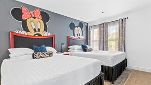 Une chambre d’hôtel avec deux lits, chacun doté d’une tête de lit à l’effigie de Mickey Mouse, une grande fenêtre avec des rideaux à motifs et un tapis noir et blanc à motifs.