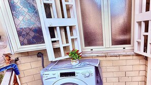 Un espace buanderie comprenant un lave-linge, une fenêtre à vitre dépolie et un carrelage décoratif sur le mur.