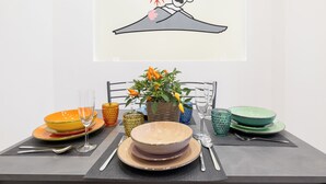Une table à manger dressée avec des assiettes, des verres et des couverts, un vase rempli de fleurs et, au-dessus, un tableau encadré.