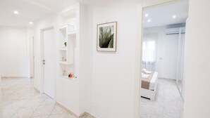 Une chambre d’hôtel moderne et minimaliste, avec un intérieur épuré et blanc, un lit, un petit coin salon et une salle de bain visible à travers une porte ouverte.