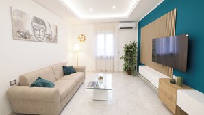 Un salon moderne avec un canapé, une table basse et un téléviseur à écran plat fixé au mur, lequel est peint dans une teinte turquoise.
