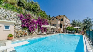 A swimming pool with lounge chairs and umbrellas, surrounded by stone walls and flowering plants. - Stunning apartment in Recco with kitchen (Recco)