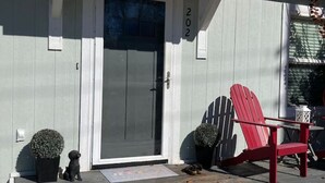 Ein Haus mit einer grauen Tür, Hausnummer 202, einem roten Adirondack-Sessel und zwei Blumentöpfen auf der Veranda.