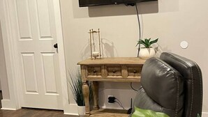 Ein Wohnzimmer mit Ledersofa, Couchtisch aus Holz, flachbildfernseher an der Wand und einer weißen Tür.