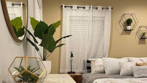 Ein Schlafzimmer mit einem Bett, einem Nachttisch, einem Spiegel, einer Topfpflanze und einem geometrischen Dekorationsobjekt.