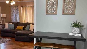 A living room with a dark wooden table and bench, a sofa, and decorative wall panels. - Easy Checkout--Safe & Comfy 3BR--King Bed--Pets OK (Rockwood)