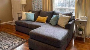 A living room with a grey sectional sofa, patterned rug, and a window with curtains. - Easy Checkout--Safe & Comfy 3BR--King Bed--Pets OK (Rockwood)