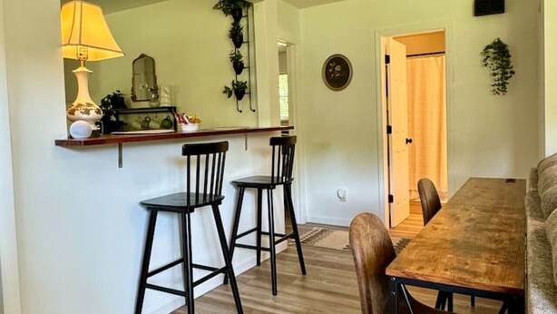 Un comedor con una mesa y sillas de madera, una pequeña zona de bar con taburetes, y un espejo en la pared.
