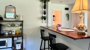 Una cocina con encimera de madera, dos taburetes negros, una planta colgante y un espejo sobre la encimera.