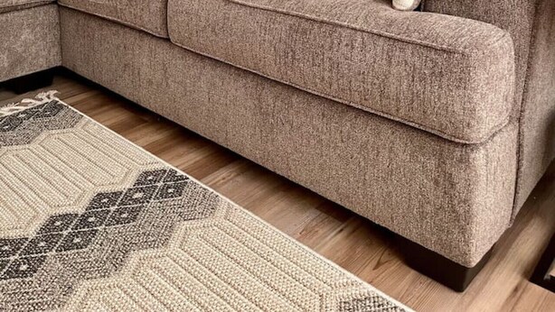 Un sofá modular con varios cojines, una alfombra estampada y un espejo montado en la pared.
