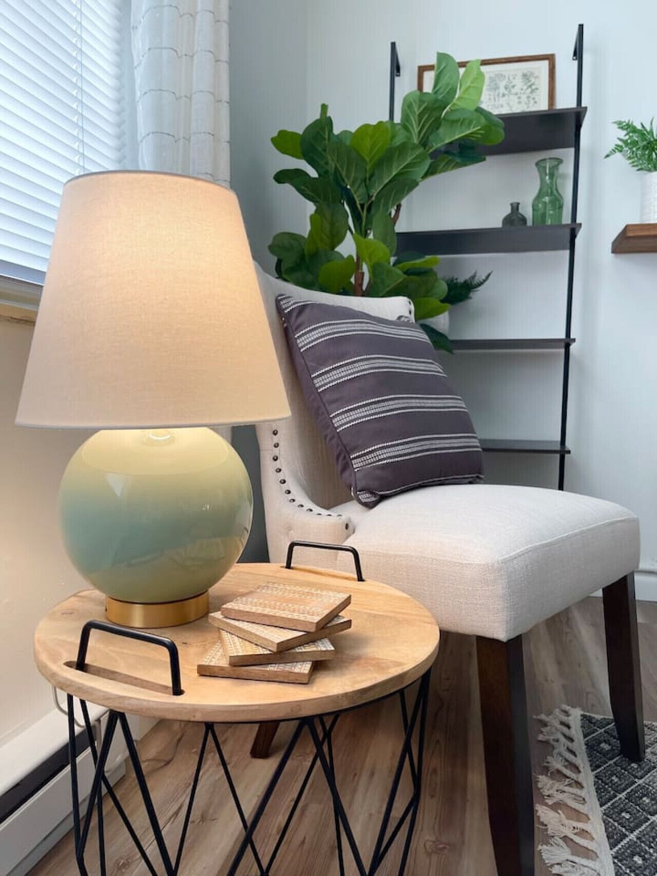 Une table ronde en bois, avec une lampe, des livres et une chaise agrémentée d’un coussin à rayures.