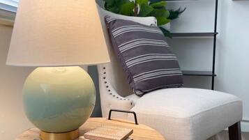 Une table ronde en bois, avec une lampe, des livres et une chaise agrémentée d’un coussin à rayures.