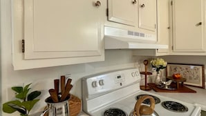 Una cocina con armarios blancos, una estufa blanca y una pequeña planta en la encimera.