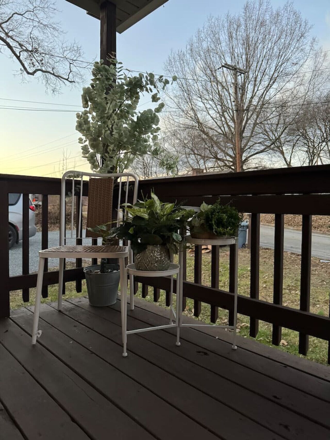 A wooden deck with a metal railing, a table, and chairs. There are potted plants on the deck.
