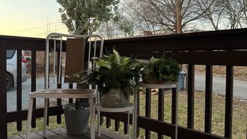 A wooden deck with a metal railing, a table, and chairs. There are potted plants on the deck.