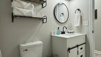 A bathroom with a toilet, sink, and towel rack. There are two towel racks with towels and a small plant.
