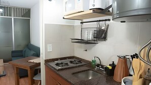 A compact kitchen with a gas stove, a sink, and a countertop. There is a small dining table and a chair. - Home in downtown-Maipu St. (Buenos Aires)